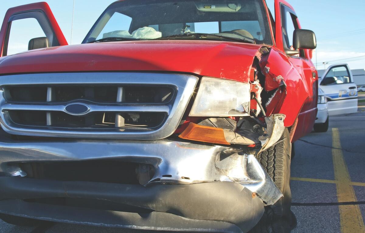 A small red pickup truck with a smashed front fender and light.