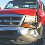 A small red pickup truck with a smashed front fender and light.