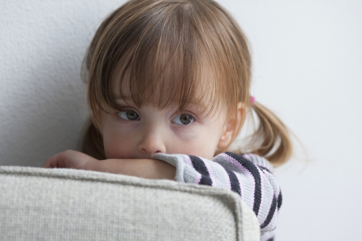 A toddler hiding behind a couch.