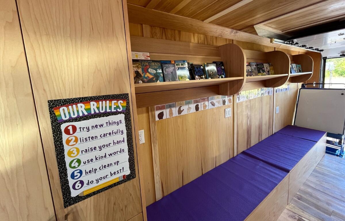 An inside look at the gus bus featuring all wood panels with bench seating and shelves full of books.