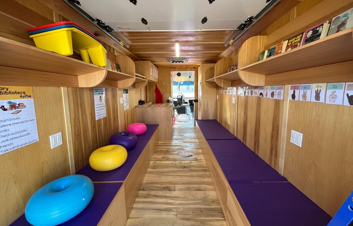 An inside look at the gus bus featuring all wood panels with bench seating and shelves full of books.