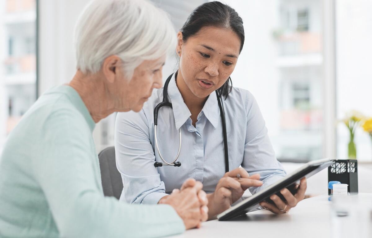A woman sitting with a nurse at a table looking at a tablet.