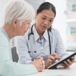 A woman sitting with a nurse at a table looking at a tablet.