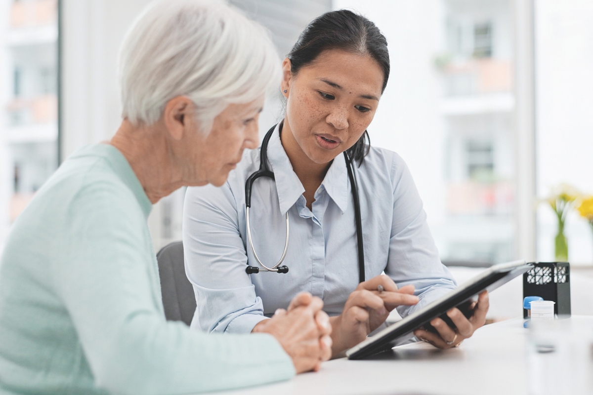 A woman sitting with a nurse at a table looking at a tablet.