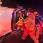Firefighters rescuing the driver of a car flipped on its side.