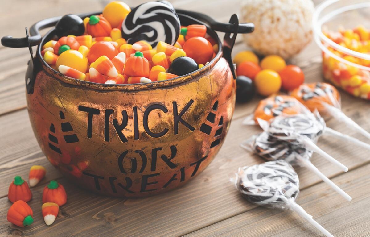 A Trick or Treat bowl full of candy corn on a table with black and white lollipops.