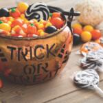 A Trick or Treat bowl full of candy corn on a table with black and white lollipops.