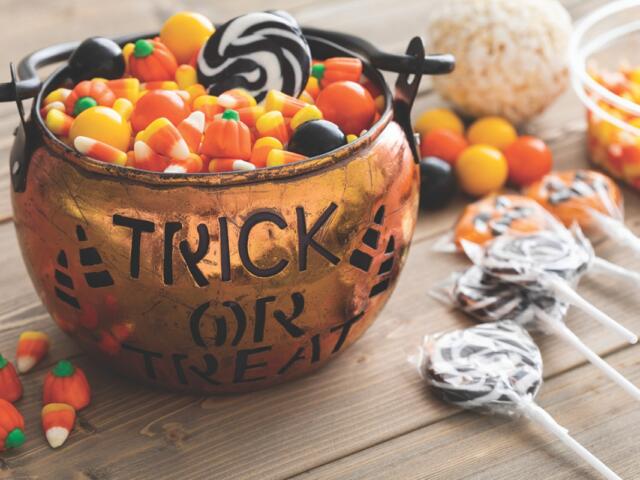 A Trick or Treat bowl full of candy corn on a table with black and white lollipops.