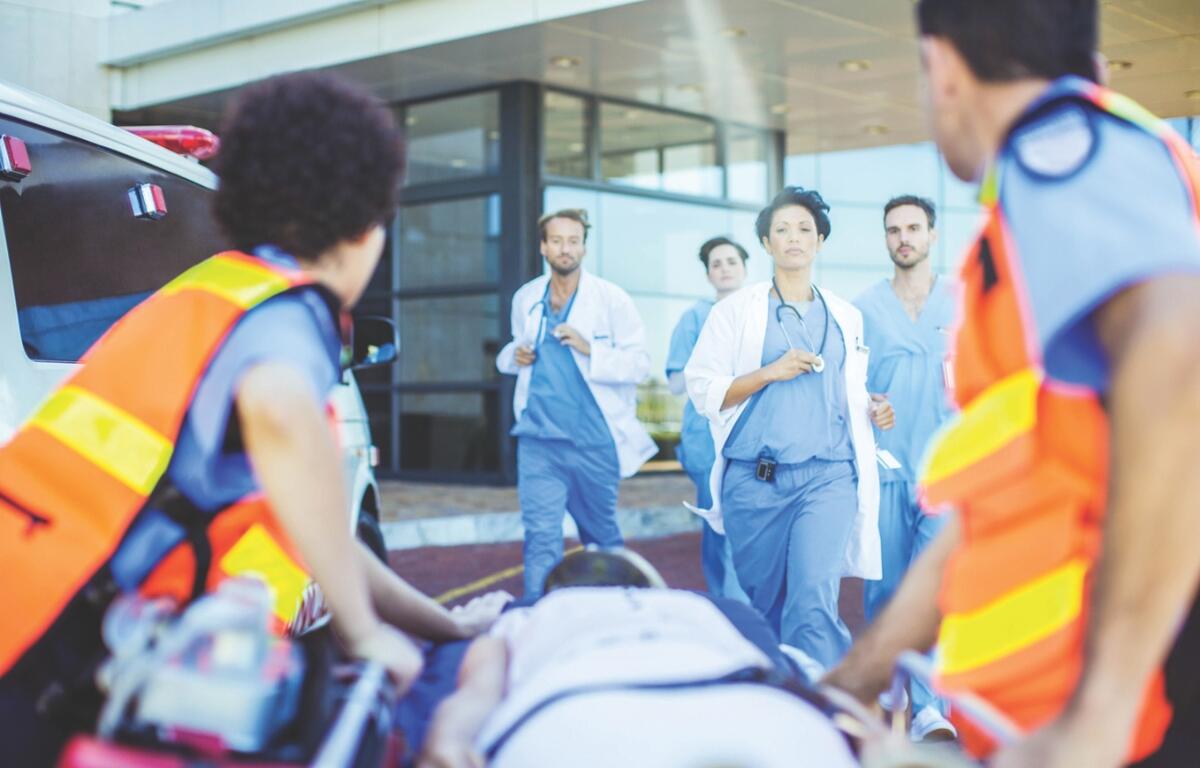 EMS personnel roll a gurney up to a hospital with doctors and nurses waiting.