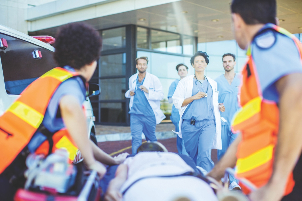 EMS personnel roll a gurney up to a hospital with doctors and nurses waiting.