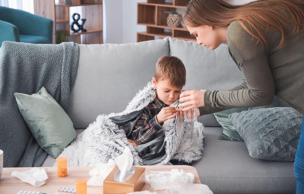Mother giving medicine to her son ill with flu at home.
