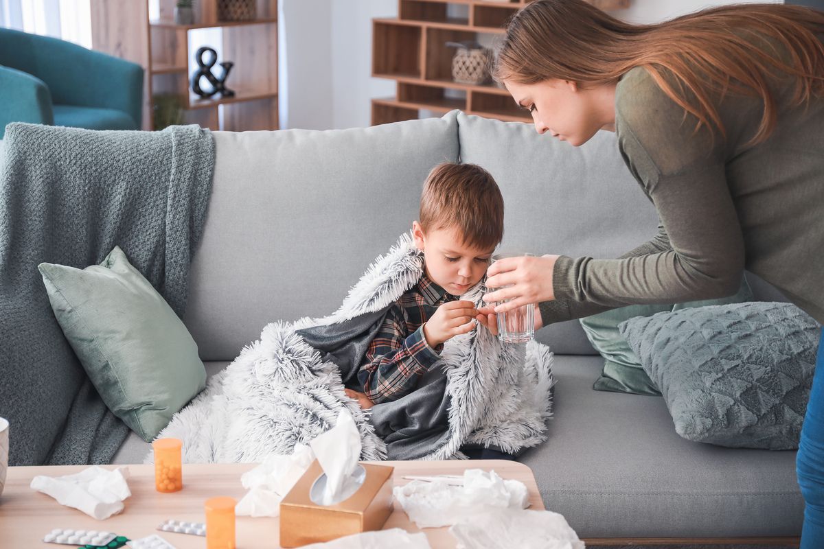 Mother giving medicine to her son ill with flu at home.