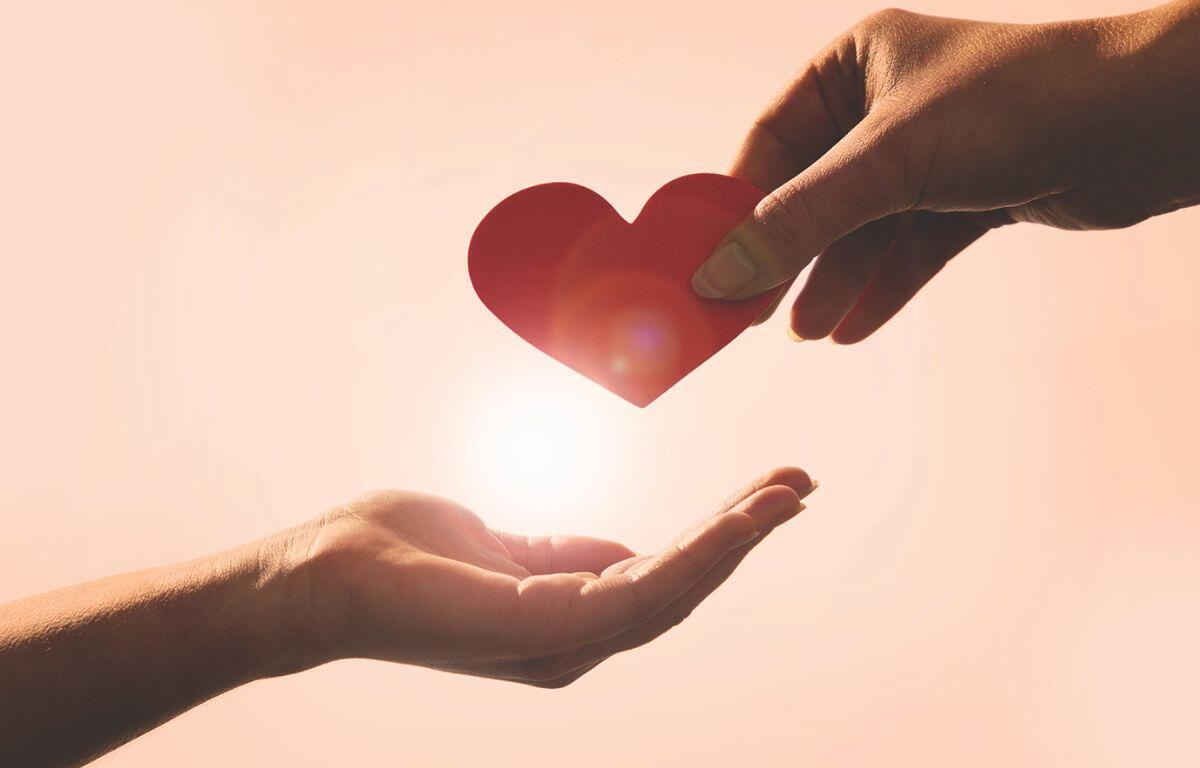 One hand giving another hand a heart