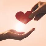 One hand giving another hand a heart