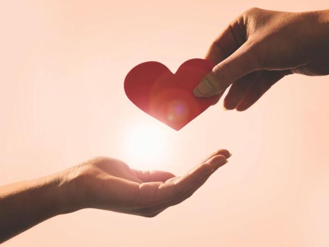 One hand giving another hand a heart