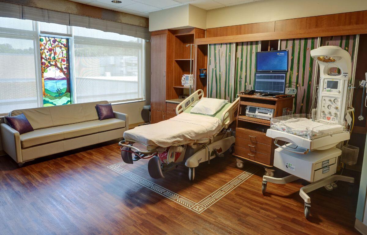 A setup for a family birthplace at Sentara with a bed, couch, medical equipment and a window.