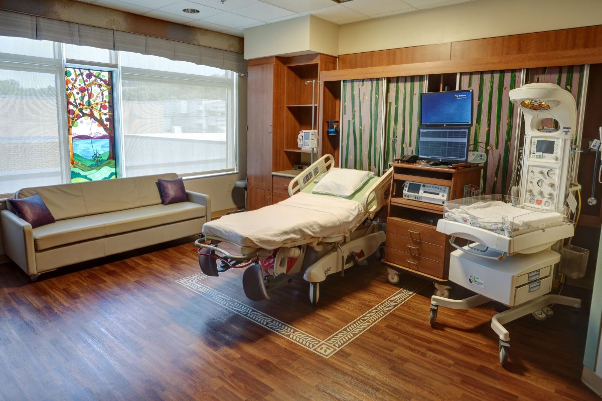 A setup for a family birthplace at Sentara with a bed, couch, medical equipment and a window.