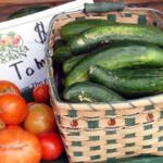 Cucumbers in a basket on a table next to tomatoes.