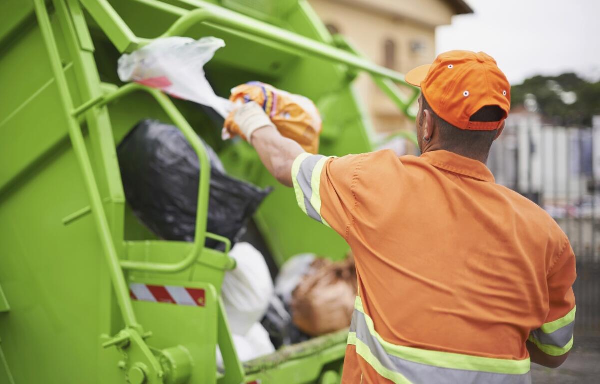 A sanitation worker throws a trash bag into a garbage truck.