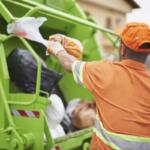 A sanitation worker throws a trash bag into a garbage truck.