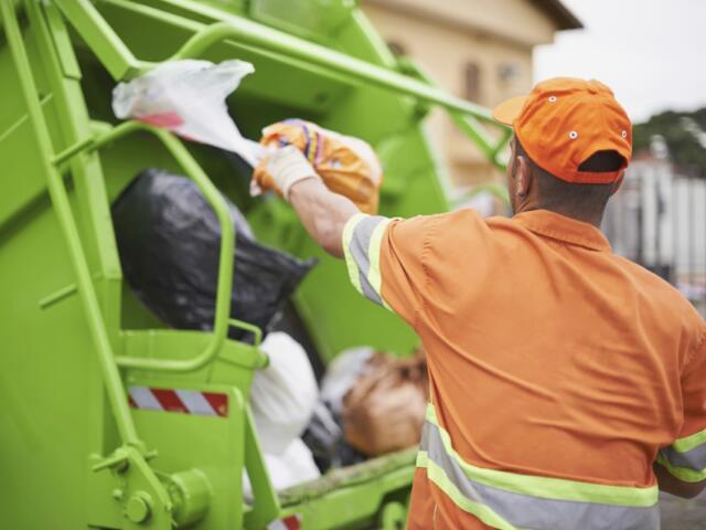 A sanitation worker throws a trash bag into a garbage truck.