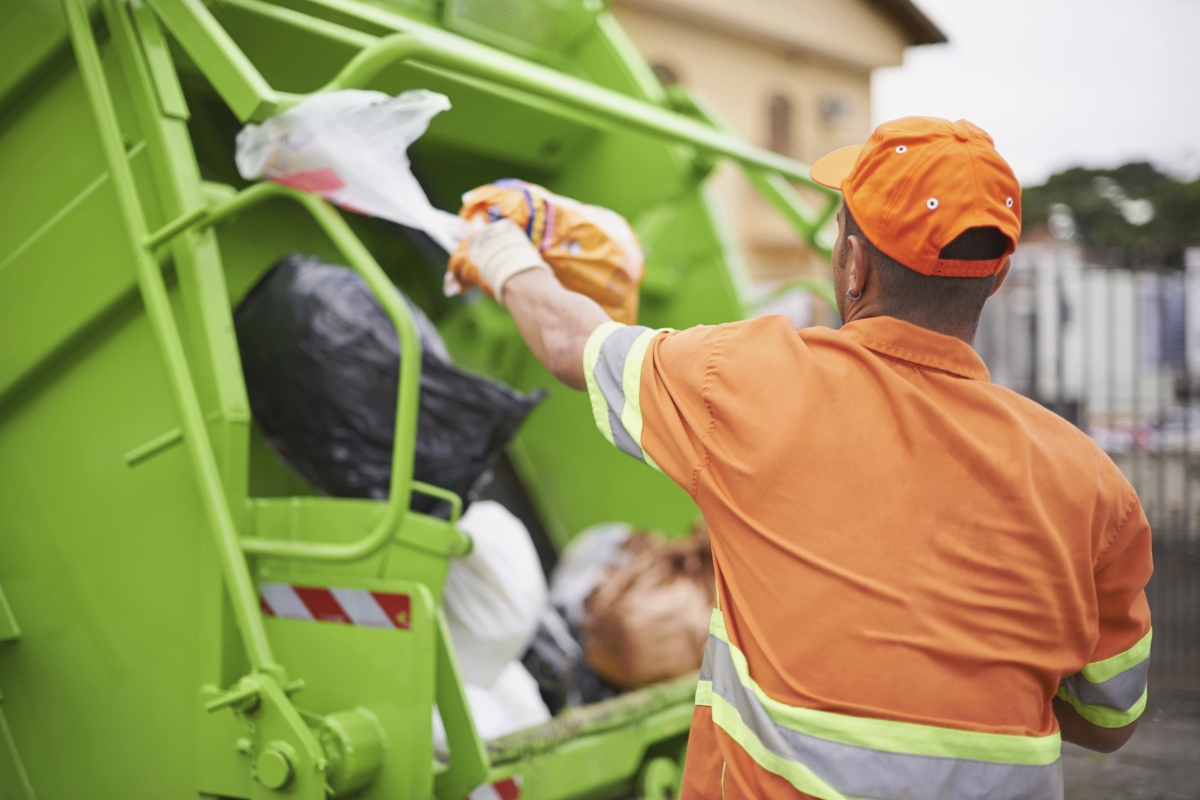 A sanitation worker throws a trash bag into a garbage truck.