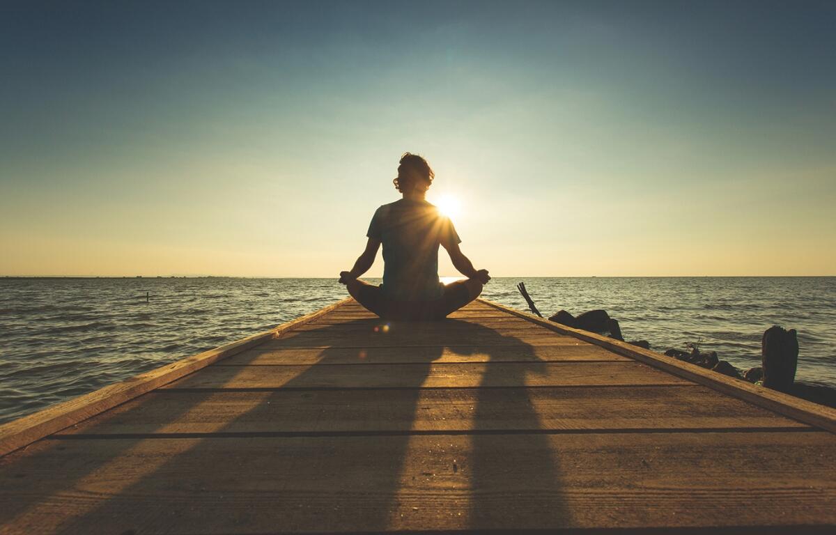 A person meditating on a pier near water.
