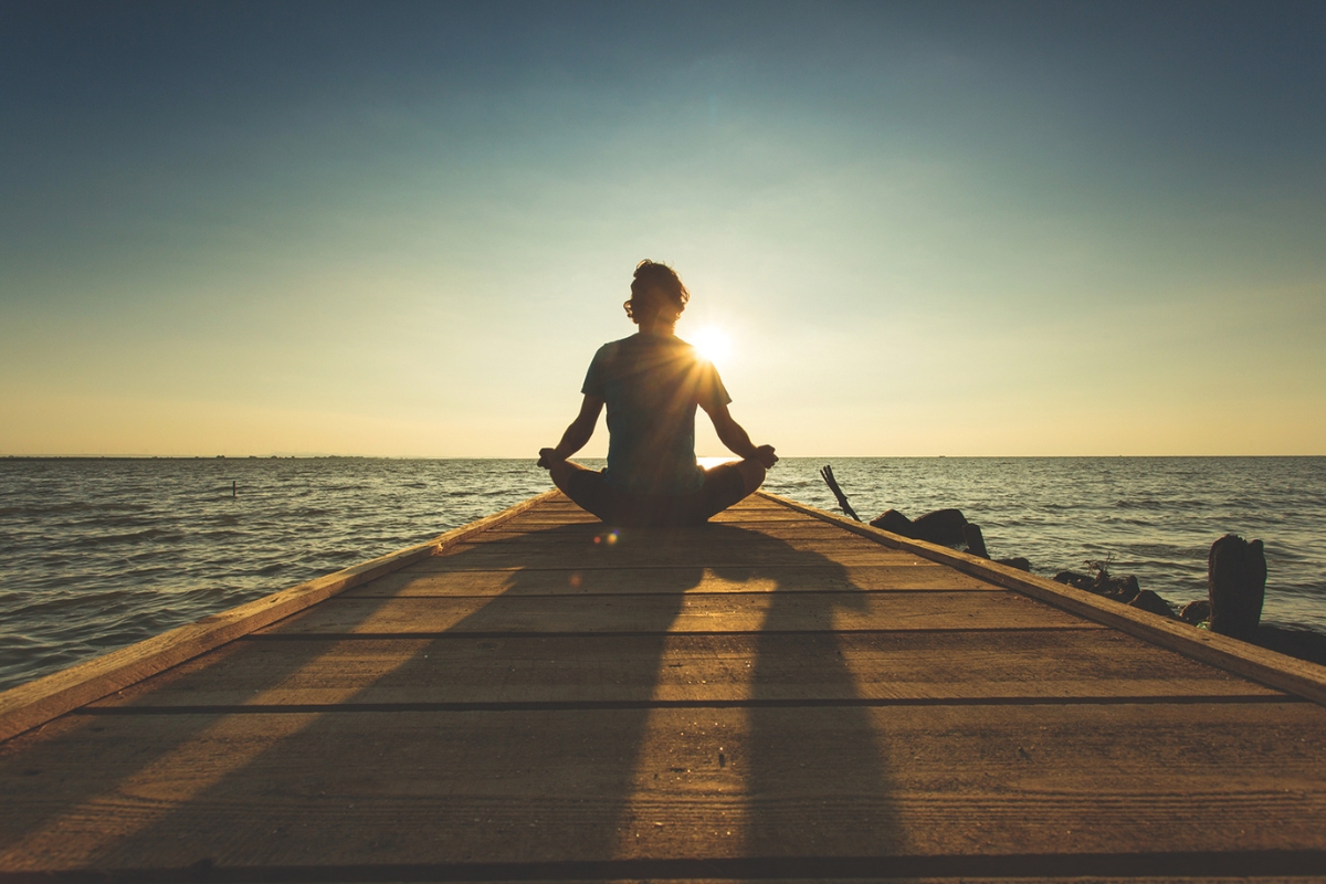 A person meditating on a pier near water.