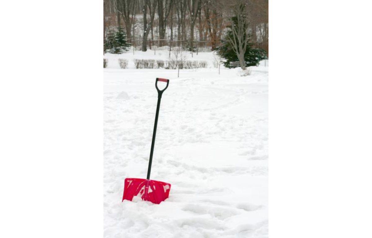 Red plastic shovel with black handle stuck in fluffy white snow.