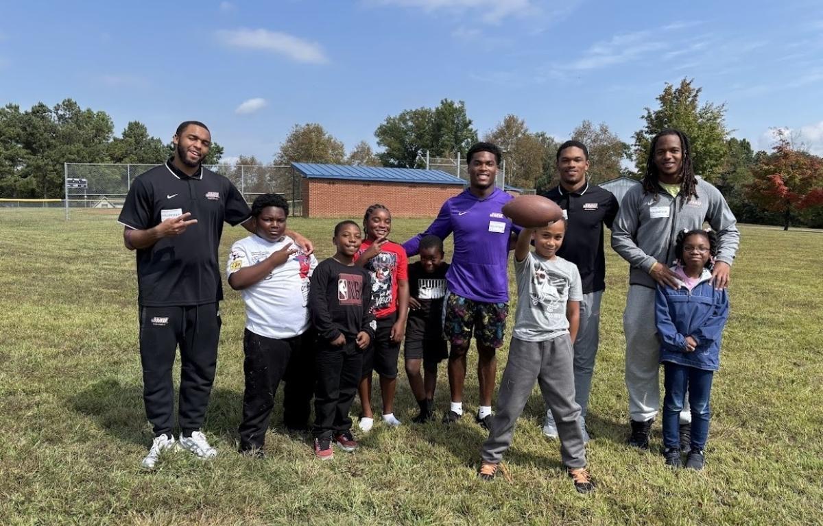 JMU football players pose with William Perry Elementary School students in the grass.