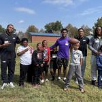 JMU football players pose with William Perry Elementary School students in the grass.