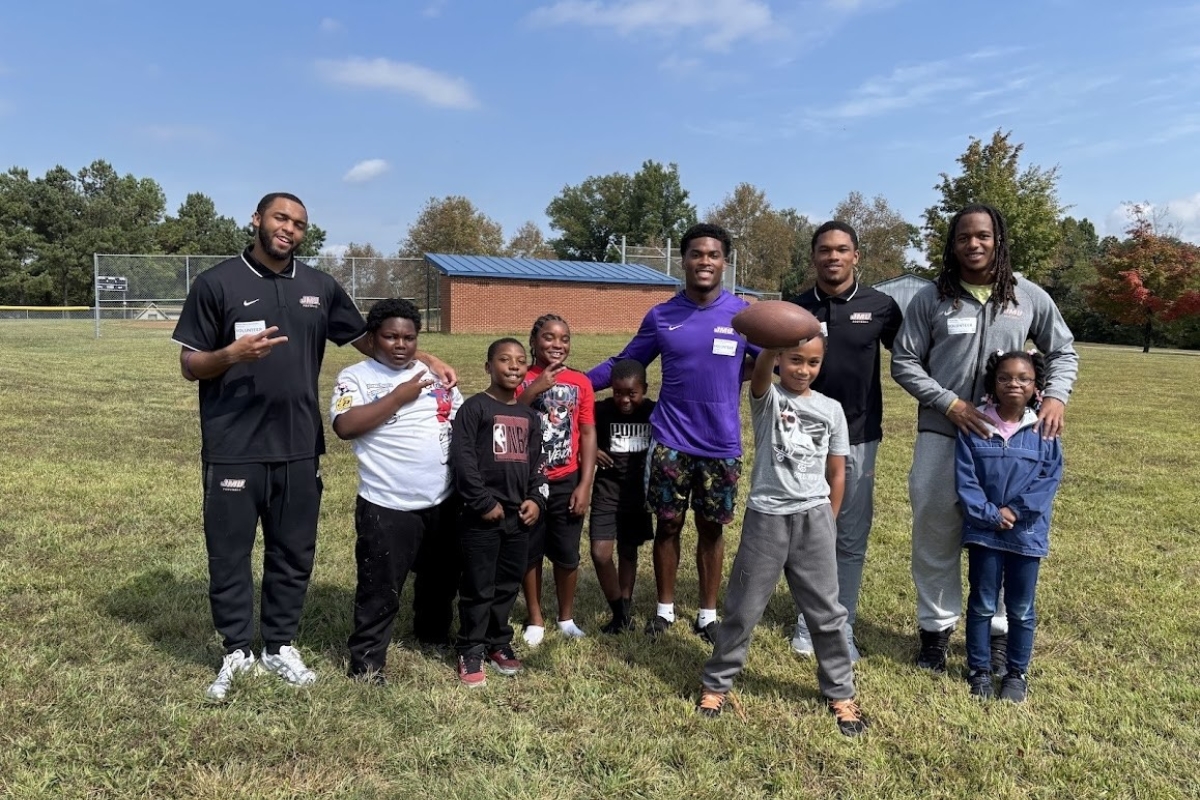 JMU football players pose with William Perry Elementary School students in the grass.
