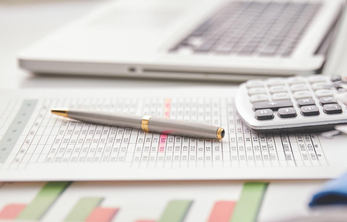 Financial papers on a desk with a laptop, pen, and calculator.