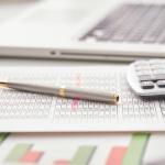 Financial papers on a desk with a laptop, pen, and calculator.