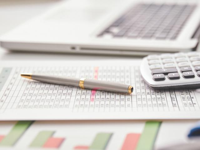 Financial papers on a desk with a laptop, pen, and calculator.