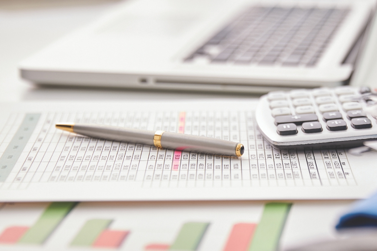 Financial papers on a desk with a laptop, pen, and calculator.