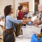 People Donating Clothing To Charity Collection In Community Center