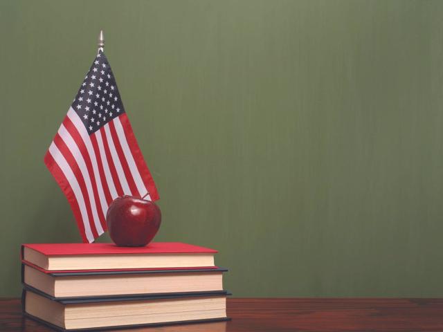 An apple on top of books with an American flag on a desk