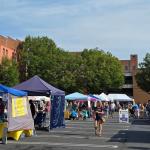 Several tent canopies set up in a parking lot with different vendors.