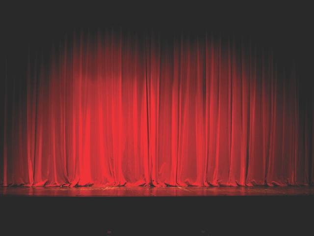 Red curtains drawn together on a stage with a spotlight.