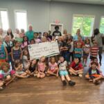A classroom of children at Living Legacy holding a giant check.