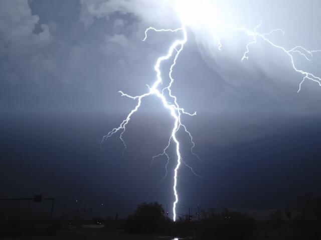 Bright lightning bolt striking from a stormy night sky onto a dark urban landscape below, streetlights silhouetted.