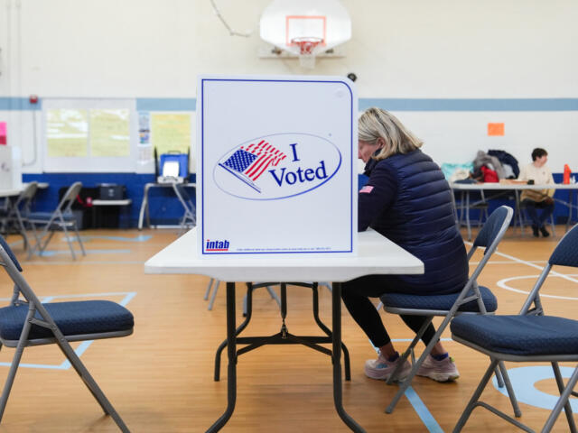 Voter seated at a table in a gym, casting a ballot at a privacy booth marked 'I Voted'.