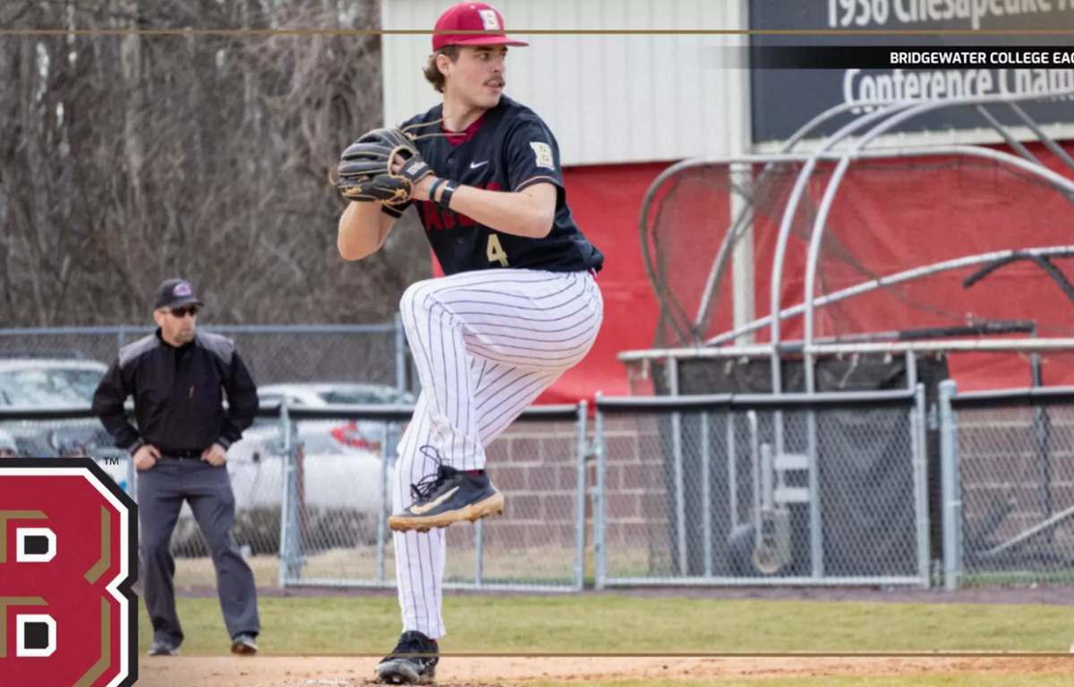 Baseball pitcher in mid-windup on the mound, wearing a black uniform and striped pants, with a large B logo in the foreground.