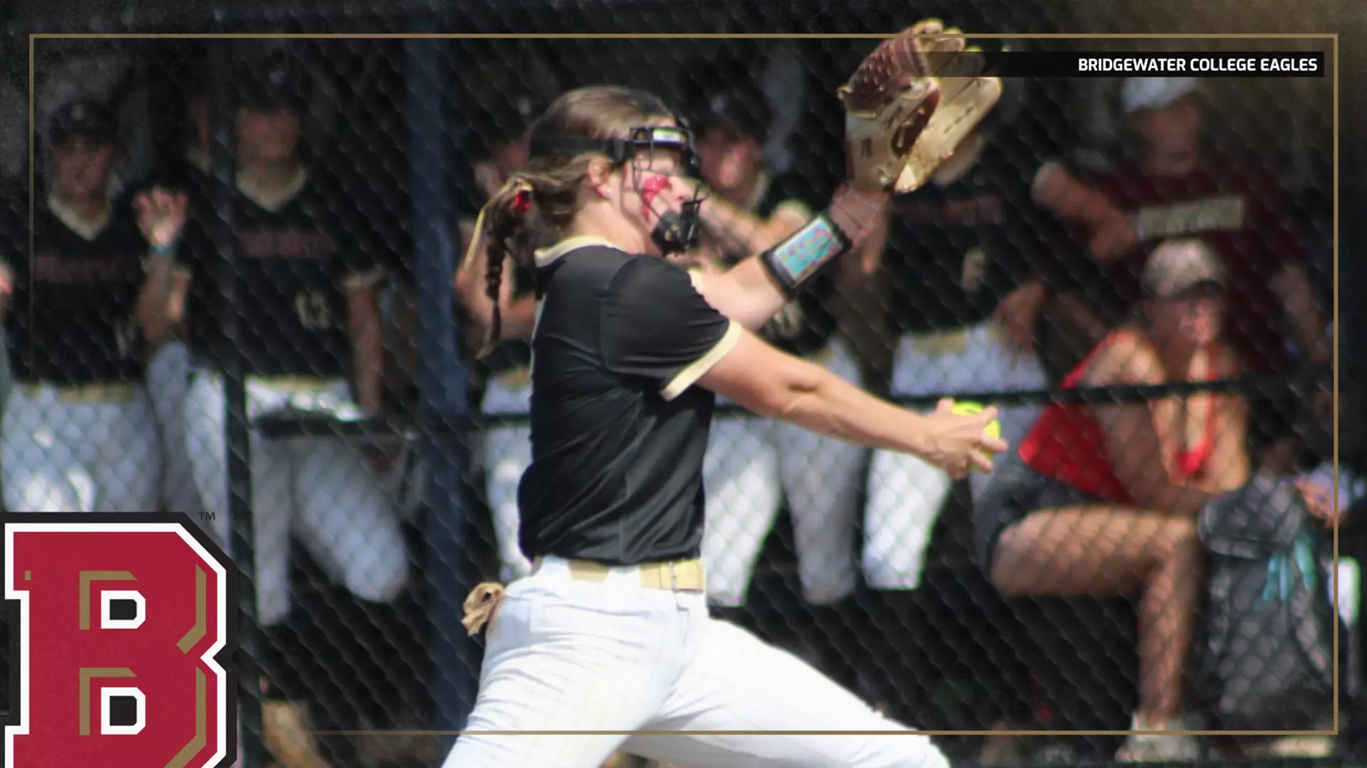 Female softball pitcher in a black shirt and white pants mid-pitch, with fans behind a chain-link fence.