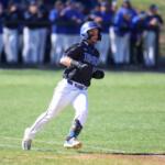 Baseball player in a dark EMU jersey running on the field, wearing a helmet and white pants with a crowd in the background. 20-23? Wait no.