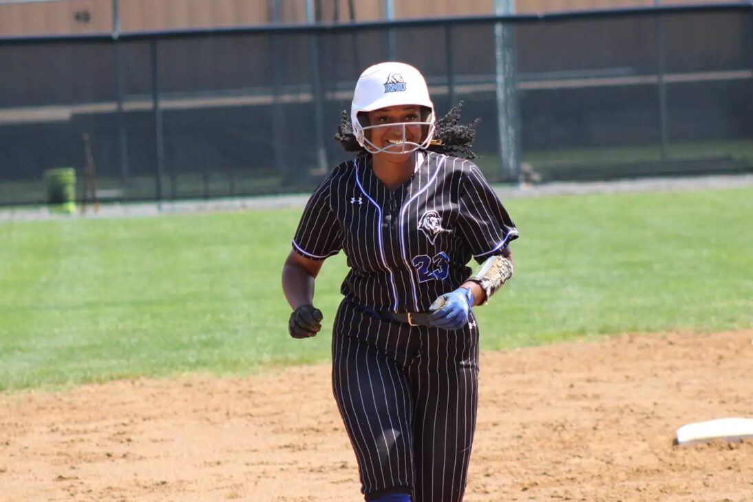 Female softball player in a pinstriped black uniform runs on the infield, wearing a white helmet and blue batting gloves.