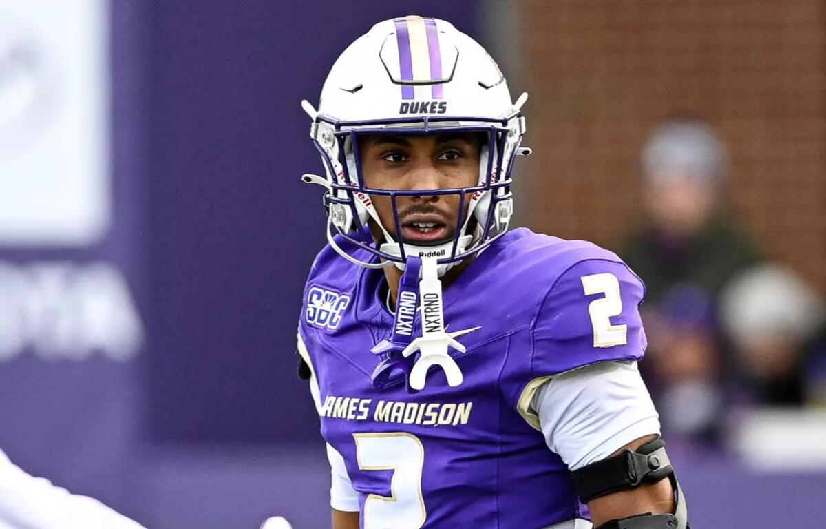 James Madison Dukes football player in a purple jersey with number 2, wearing a white helmet labeled DUKES, looking sideways on the field.