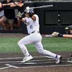 Baseball batter in white pinstripe uniform swings at a pitch as the catcher in black crouches behind home plate during a game in progress.