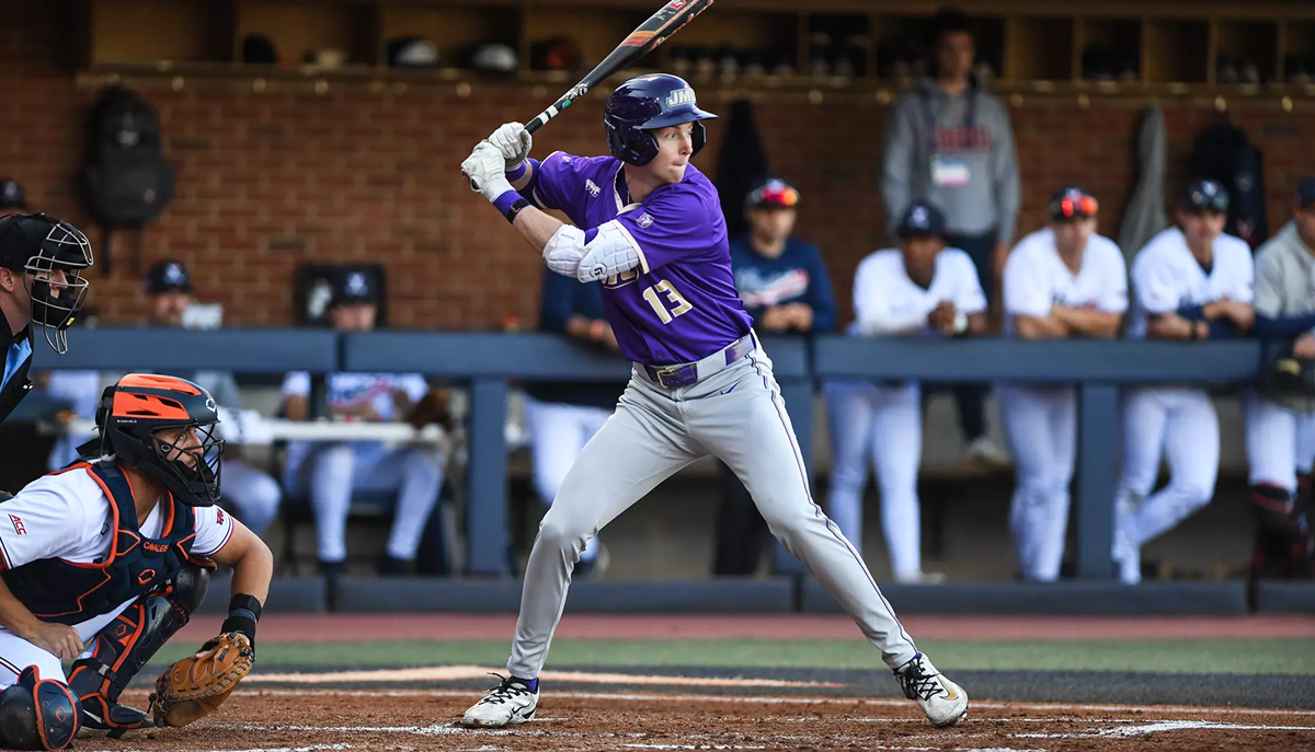 Baseball batter in purple jersey swinging at a pitch, with catcher behind home plate and umpire nearby